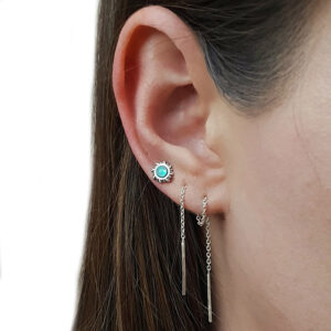 A close-up of an ear with a mint green faux opal silver stud earring and two dangling silver chain earrings.