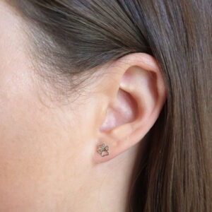 A close-up of an ear with 🐾 Cutout Dog Paw Sterling Silver Earring Studs, brown hair partly visible.