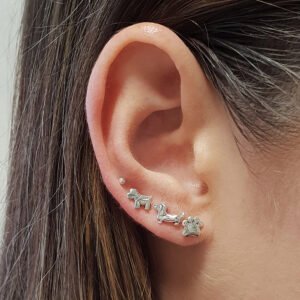 A close-up of an ear wearing 🐾 Cutout Dog Paw Sterling Silver Earring Studs, with straight brown hair in view.