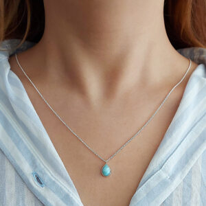 A woman wears the 💧 Larimar Tear Drop Gemstone on Fine Silver Chain Necklace with a light blue striped shirt.