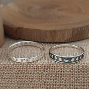 Two Phases of the Moon Silver Rings rest on textured fabric near a circular wooden object.