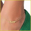 A gold anklet with the word love on it, worn on an ankle with a green shoe.