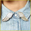 Close-up of a denim shirt collar with silver wing-shaped pins on each side of the collar points.
