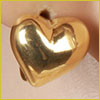 A shiny gold heart-shaped pendant resting on light-colored skin, reflecting light.