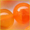 Two shiny orange marbles resting on a soft, textured surface with a warm, light-orange background.