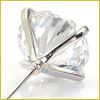 Close-up of a clear faceted gemstone set in a silver prong setting with a pin extending from the base.
