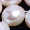 Close-up of shiny, oval-shaped white pearls strung together against a black background.