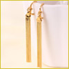 Gold-tone long rectangular dangle earrings hanging on the rim of a white cup, against a light background.