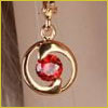 Gold earring with a circular design, holding a single round red gemstone at the center, shown against a neutral background.