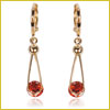 Gold earrings with teardrop-shaped wire and a small red gemstone suspended at the bottom, set against a white background.