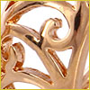Close-up of an intricate, shiny gold metal design with swirling, decorative patterns on a light background.