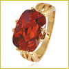 Gold ring with a large oval red gemstone, set in a pronged setting with decorative band details.