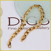 A gold chain bracelet is displayed on a surface with partially visible text and a round glass object nearby.