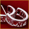 Silver hoop earrings with Roman numerals carved into them, displayed on a red fabric background.