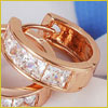 Close-up of two gold hoop earrings with square-cut clear gemstones set in a row, placed on a light background.