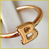 A gold ring with the letter B on it resting against a white fabric background.