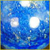 Close-up of a polished blue stone with white and gold flecks, possibly lapis lazuli, reflecting light.