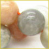 Close-up of several round, smooth beads in shades of gray, peach, and white, partially overlapping each other.