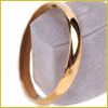 A shiny gold bangle bracelet displayed on a light gray stand.
